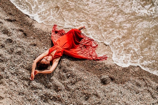 Woman red dress sea. Female dancer in a long red dress posing on a beach with rocks on sunny day.