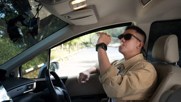 Young man sitting at the wheel of a car and drinking water from a plastic bottle. Traveling and lifestyle concept.