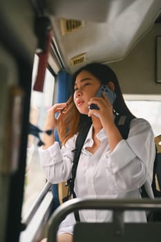 Happy young woman sitting inside public bus transport and talking on mobile phone.