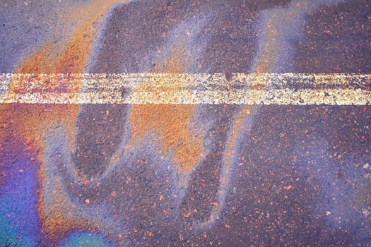 Oil spill on wet asphalt, parking lot with dividing line.
