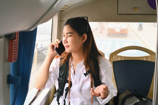 Happy young Asian woman talking on mobile phone while while traveling in bus. Travel lifestyle and transportation concept.