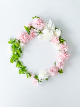 Round frame of pink and white carnations, green leaves, gypsophila on a white background. Flat lay, top view. Spring background. Suitable for wedding, cards and invitations