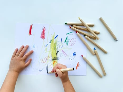 small child draws with colored pencils on paper on white table. High quality photo