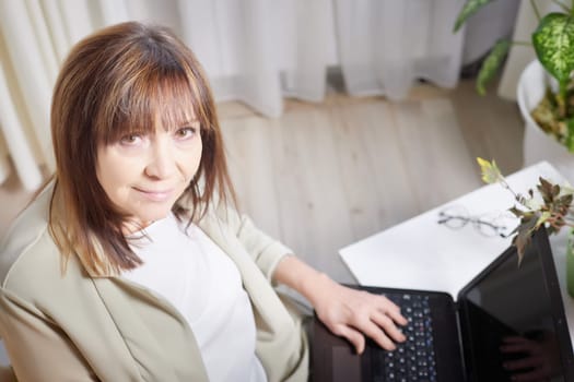 Elderly lady with a laptop in the room. A businesswoman is a leader, a manager is working. Grandma communicates with her grandchildren on the Internet