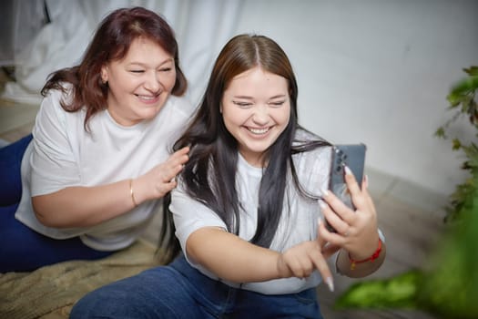 Fat funny funny adult mother and daughter posing, taking selfies indoors. Body positive, friendly family in the room