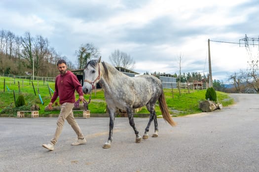 Man walking a horse with a rope at an equestrian center in a cloudy day