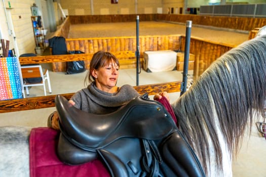 High angle view of a woman saddling a horse in stable