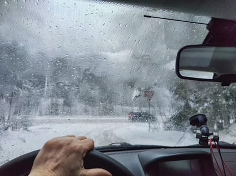 Hand of woman on steering wheel in car and and forest with cloudy windshield, fogged with snow ice in winter. Blurred woman driving car in travel