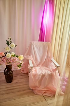 Delicate pink bright interior of the room with an armchair, vase with roses, draped curtains and a window. Location and background in the photo studio