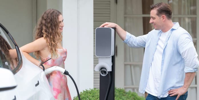 Happy and lovely couple with eco-friendly conscious recharging electric vehicle from EV home charging station. EV car technology for home utilization to future sustainability. Panorama Synchronos