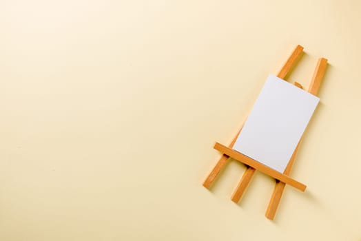 Small wooden easel with blank photo card on yellow background