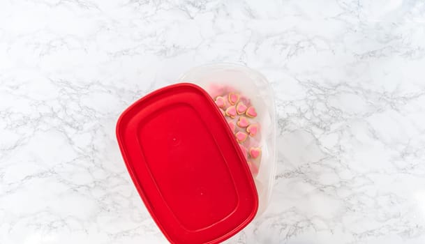 Flat lay. Storing heart-shaped sugar cookies with pink and white royal icing in a large plastic container.