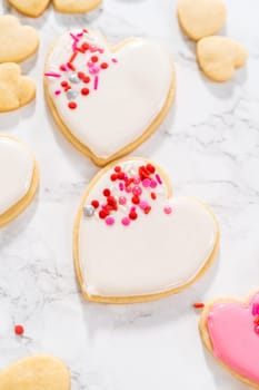 Decorating heart-shaped sugar cookies with pink and white royal icing for Valentine's Day.