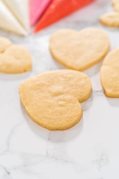 Decorating heart-shaped sugar cookies with pink and white royal icing for Valentine's Day.