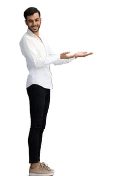 A young man on a white background in full growth shows his hand to the side.