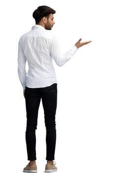 A young man on a white background in full growth shows his hand to the side.