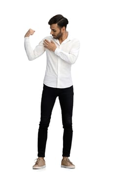 A young man on a white background in full growth demonstrates strength with his hands.