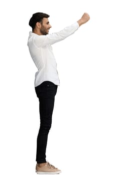 A young man on a white background in full growth raised his hands in the air, in profile.