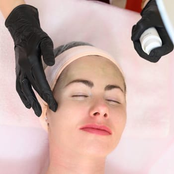 Ivano-Frankivsk, Ukraine May 17, 2023: A beautician applies a green mask to a girl's face, carboxytherapy cosmetology procedure, a beautician in black gloves.