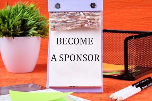 BECOME A SPONSOR text written on the page of the desktop calendar on an orange background