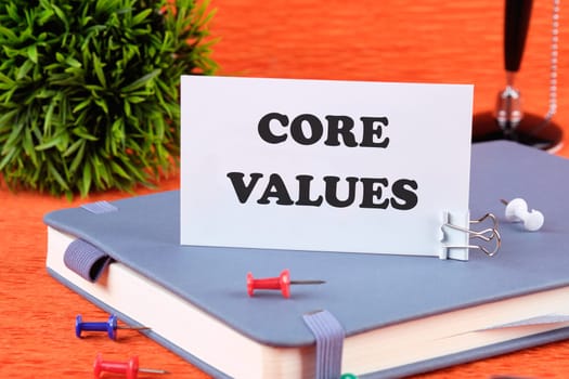 CORE VALUES word written on a business card standing with a clip on a diary, a notebook on an orange background