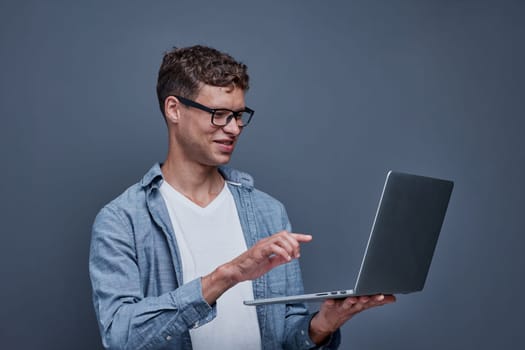 young man on gray background holding a laptop.