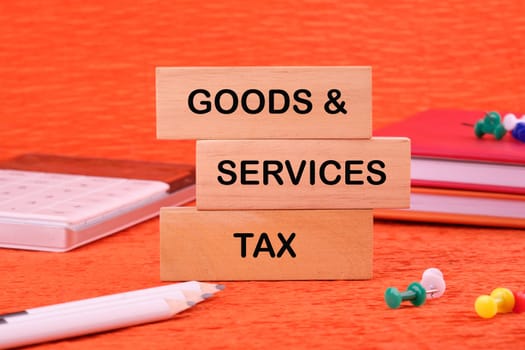 Goods and services and tax text written on a wooden block on an orange background next to office supplies