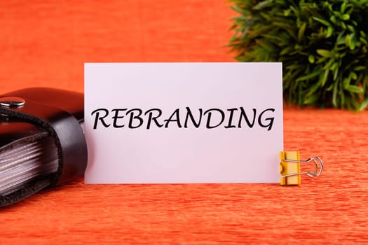 rebranding word written on a white card near the business card holder in black on an orange background