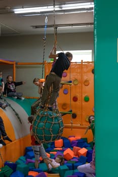 Ivano-Frankivsk, Ukraine June 7, 2023: A child rides on a rope over a pool of soft cubes, children's entertainment in a playroom.
