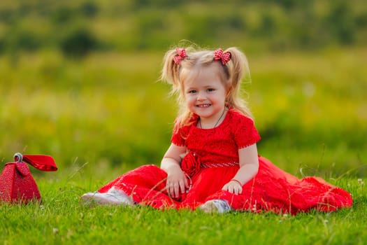 little girl in a red dress sits on a green lawn