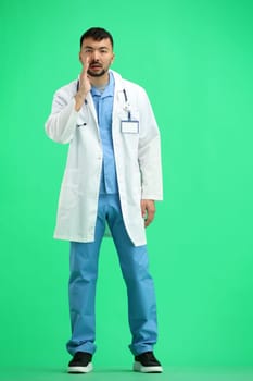 The doctor, in full height, on a green background, tells a secret.