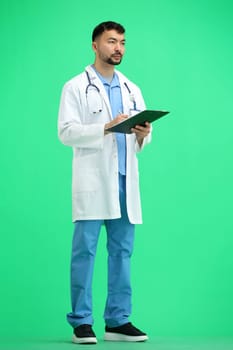 The doctor, in full height, on a green background, writes.