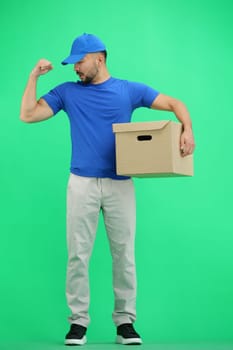 The deliveryman, in full height, on a green background, with a box, shows strength.