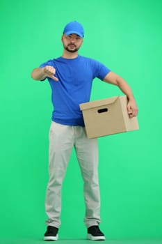 The deliveryman, in full height, on a green background, with a box, shows his finger down.