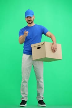 The deliveryman, in full height, on a green background, with a box, points forward.