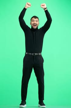 A man, on a green background, in full height, raised his hands.