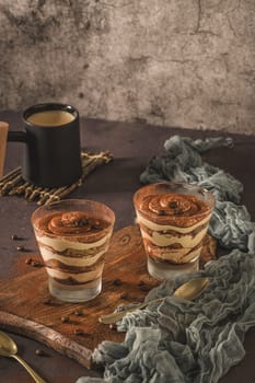 Delicious italian dessert tiramisu in a glasses on a dark slate, stone or concrete background.