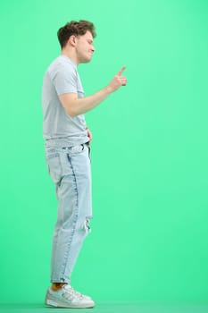 A man, full-length, on a green background, points to the side.