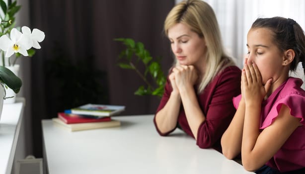Religious Christian girl praying with her mother indoors.