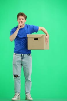 The deliveryman, in full height, on a green background, with a box, shows a sign of silence.