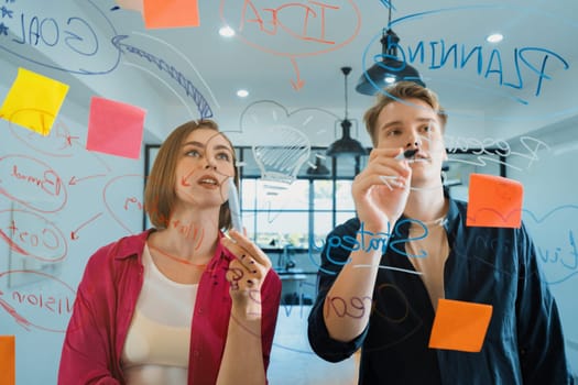 Couple of young creative start up business people brainstorming idea and solving problems by using sticky note and mind map at glass board, meeting room. discussing, working together. Immaculate.