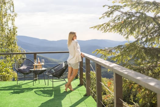 Young beautiful woman enjoys mountain view from a terrace. Freedom concept. Travel and tourism
