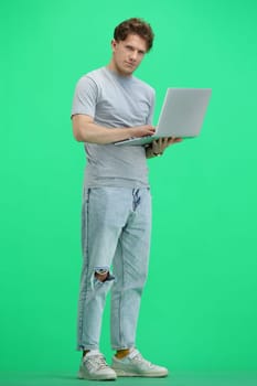 A man, full-length, on a green background, with a laptop.