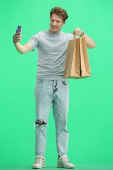 A man, full-length, on a green background, with bags and a phone.