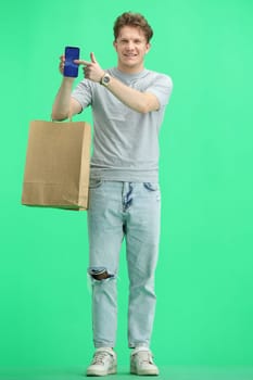 A man, full-length, on a green background, with bags and a phone.