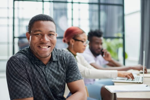 young African American man posing for the camera while sitting at a table in front of his colleagues