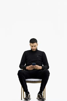 A man, full-length, on a white background, sitting on a chair.