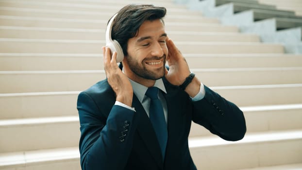 Closeup image of professional business man enjoy to listen music by using headphone. Portrait of skilled project manager show facial expression about joy and happy while sitting at mall. Exultant.