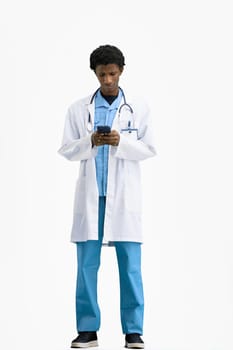 The doctor, in full height, on a white background, uses a phone.