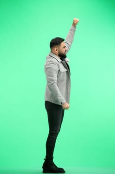 A man, full-length, on a green background, raised his hand up.